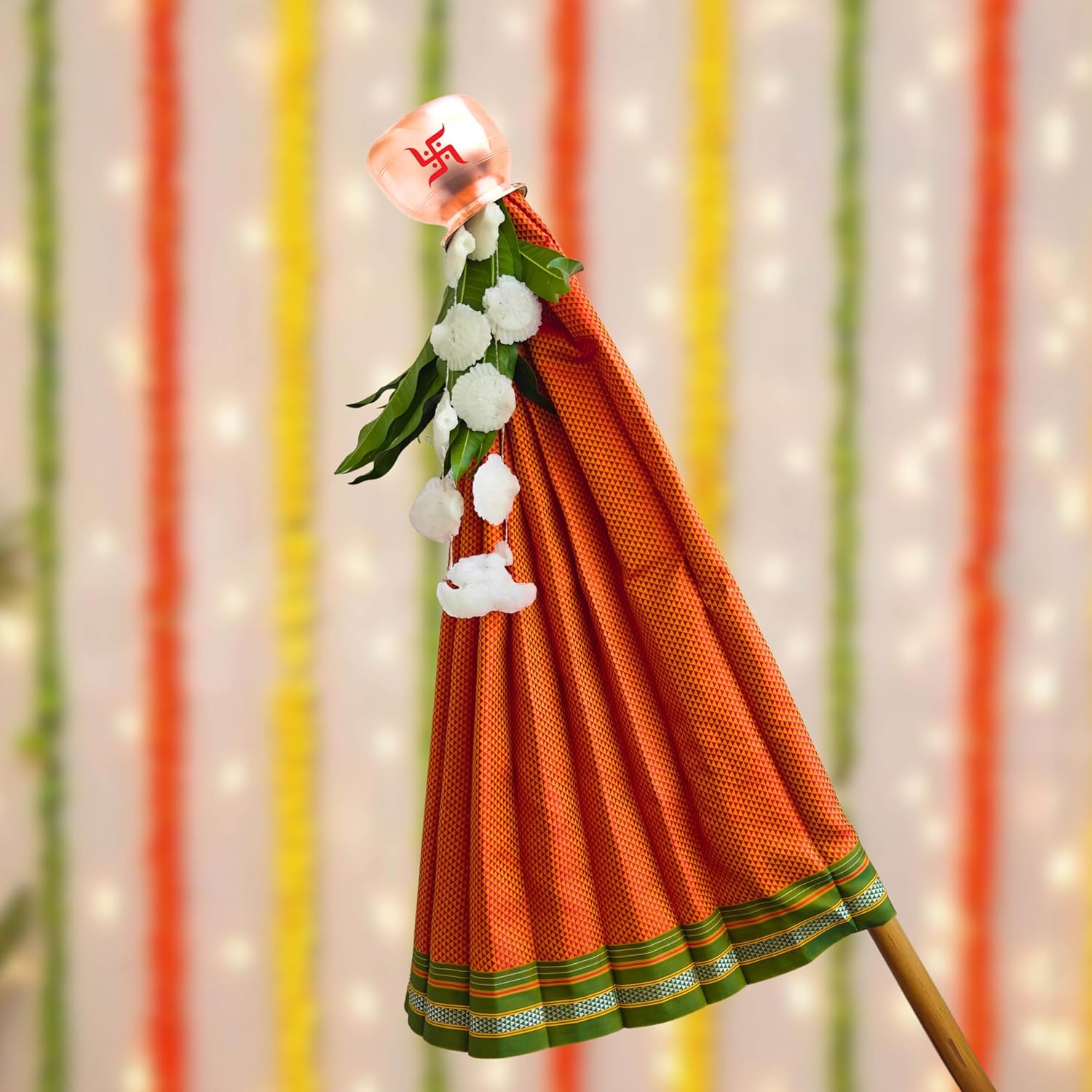 Traditional orange saree with green border hanging against a colorful striped background