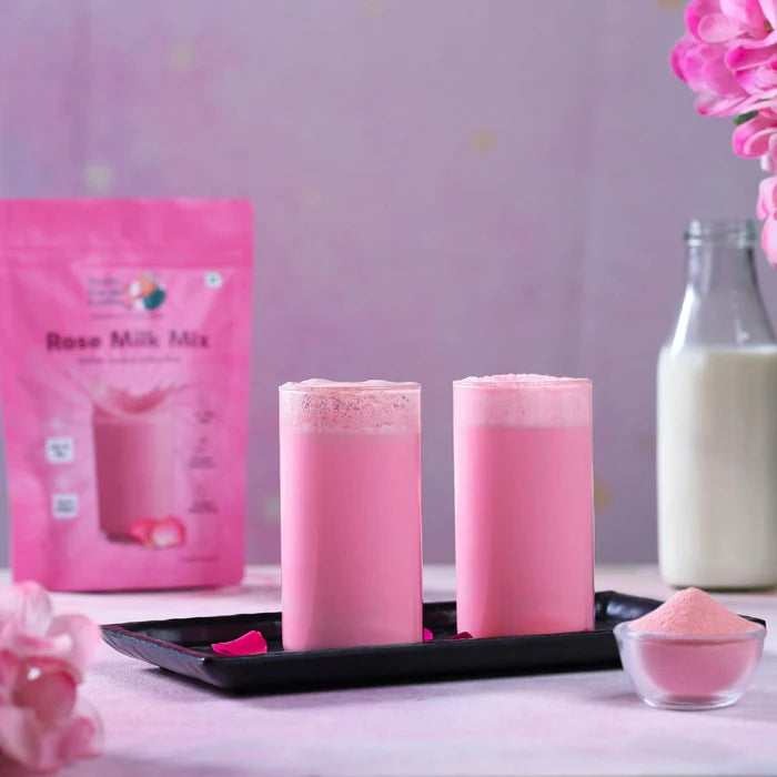 Two pink milk drinks with a package of Rose Milk Mix on a table.